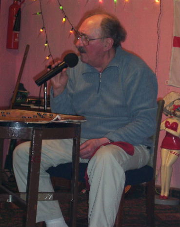 Gordon Cragg seated at bingo board with red bag containing the bingo numbers on his lap